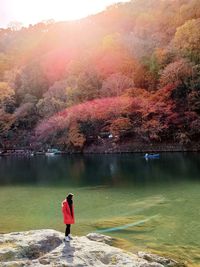 Rear view of person standing by lake during autumn