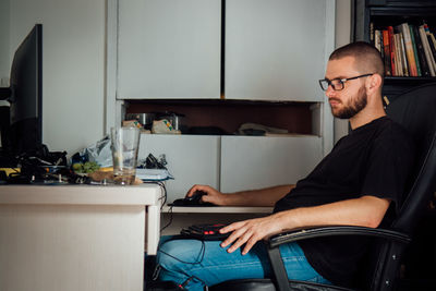 Side view of young man using computer while on chair at home