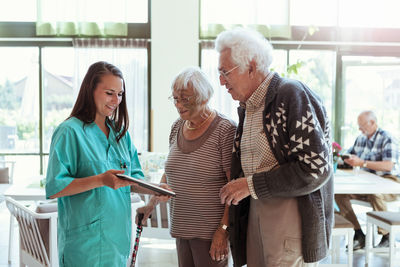 Young caretaker showing digital tablet to senior couple at nursing home