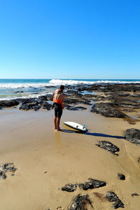 Rear view of man walking on beach against clear blue sky