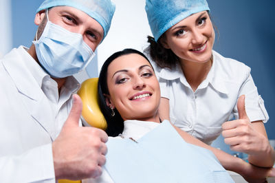 Portrait of confident doctors with patient showing thumbs up in dental clinic