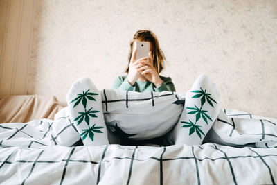 Young woman using mobile phone while sitting on bed at home