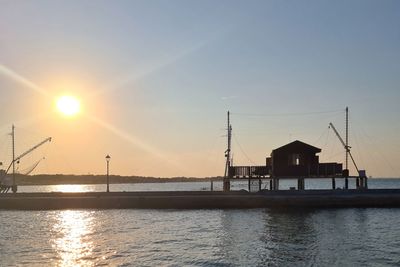 Silhouette buildings by sea against sky during sunset