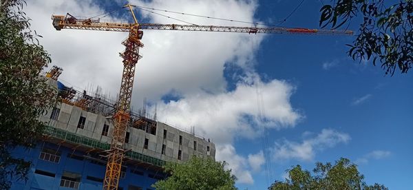 Low angle view of crane by building against sky