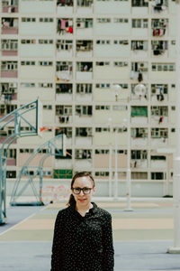 Portrait of woman wearing eyeglasses while standing against building during sunny day