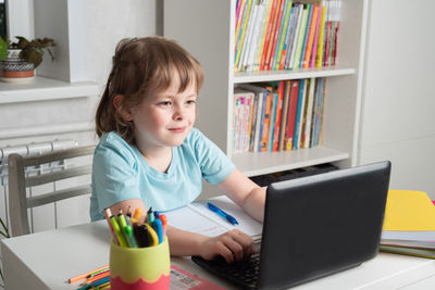 Happy girl sits at a table with books and works on a laptop. children learning at home. 