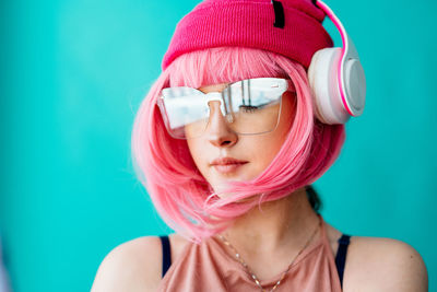 A teenager in headphones with pink hair.  a girl with a short haircut on a blue background.