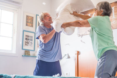 Low angle view of senior couple pillow fighting at home