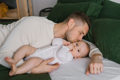 Dad's kiss of his six-month-old son lying on the bed at home