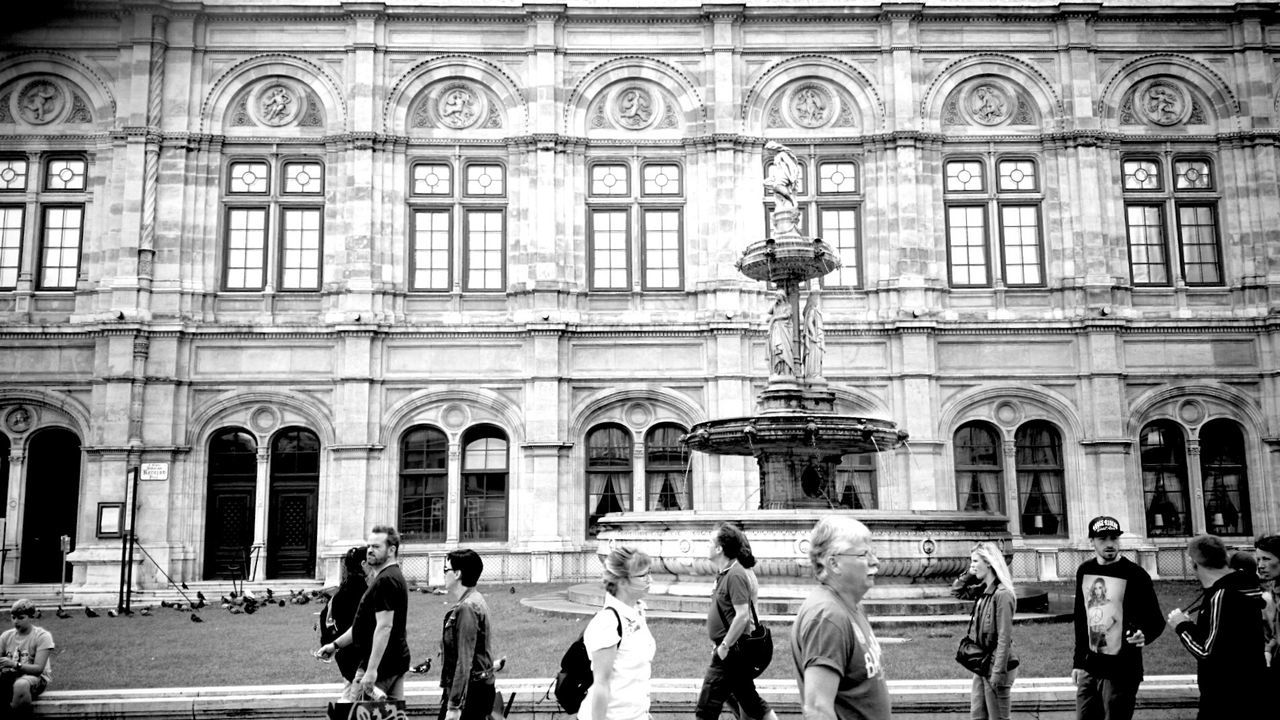 architecture, building exterior, large group of people, men, built structure, person, lifestyles, walking, city, street, city life, leisure activity, facade, day, outdoors, arch, building, full length, street light