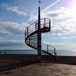 Low angle view of steps against sea and cloudy sky on sunny day