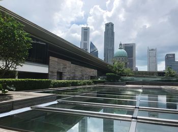Modern buildings by swimming pool against sky in city