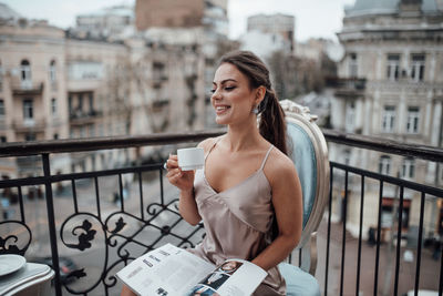 Young woman smiling while standing against railing in city