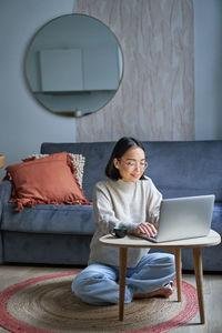 Young woman using laptop while sitting on sofa at home