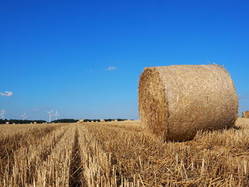 Hay bales on field against blue sky