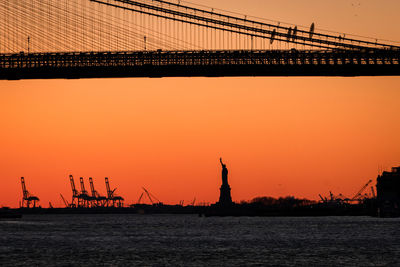 Low angle view of silhouette bridge and statue of liberty against sky during sunset 