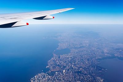 Cropped image of airplane flying over sea and cityscape