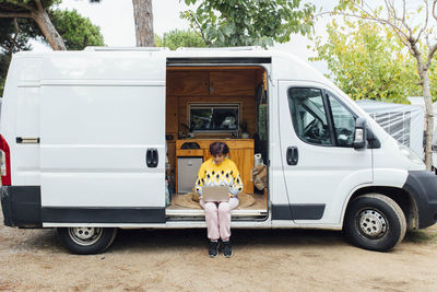 Middle-aged woman sitting with laptop in camper van while working. nomad life.