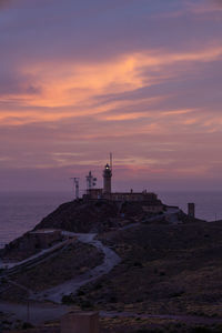 Lighthouse by sea against sky during sunset