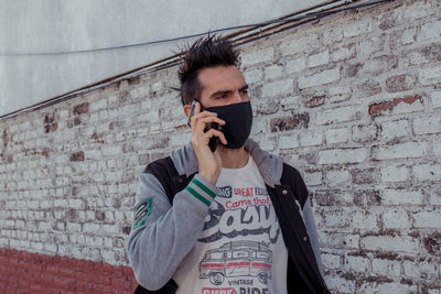 Young man using mobile phone against wall