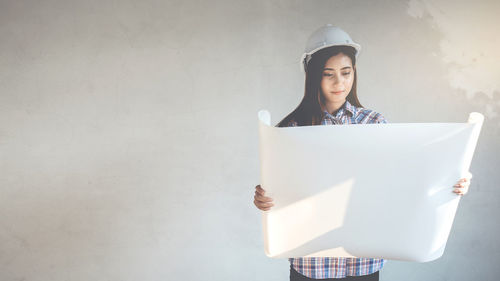 Young engineer analyzing blueprint while standing against wall