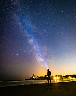 Silhouette of man star gazing on the beach under the milkyway galaxy.