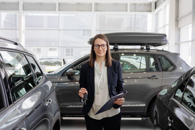 Portrait of young woman standing against car