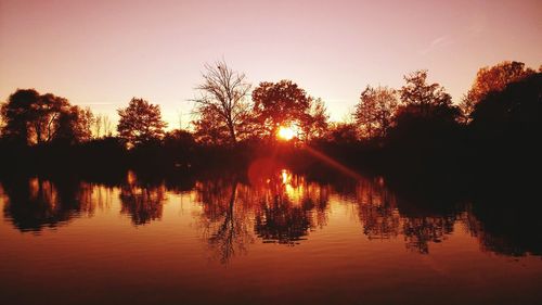 Silhouette trees by lake against sky during sunset