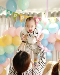 Mother carrying toddler against balloons during birthday celebration