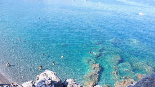 High angle view of rocks by people swimming in sea