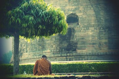 Rear view of man sitting against wall