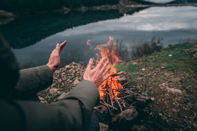 Midsection of woman by fire and lake against sky