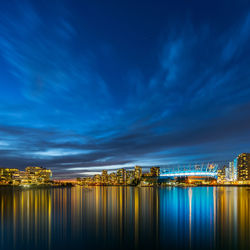 Illuminated city by river against sky at night