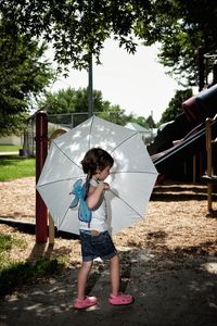 Side view of girl with umbrella walking on field at park
