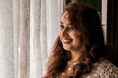 Close-up of happy young woman by curtain