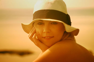 Portrait of young woman wearing hat at beach during sunset