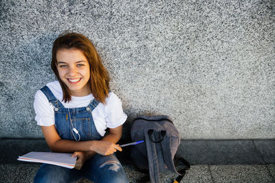 Portrait of smiling young woman sitting against wall