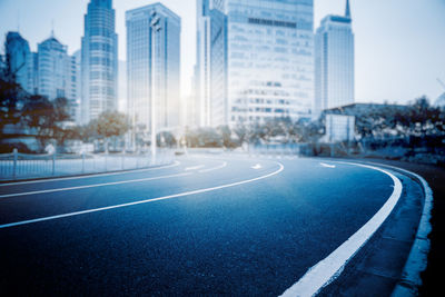 Road by buildings in city against blue sky