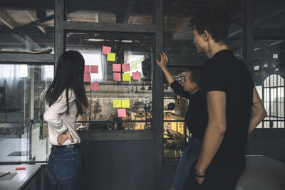 Male an female coworkers reading sticky notes on glass door at workplace