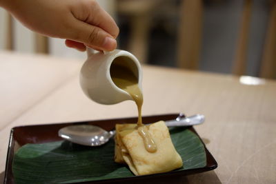 Close-up of hand pouring dessert sauce on pancake