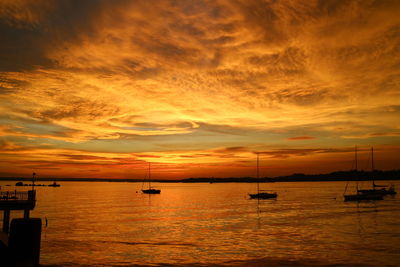 Silhouette boats moored on sea against orange sky