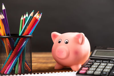 Close-up of piggy bank with school supplies on table against black background