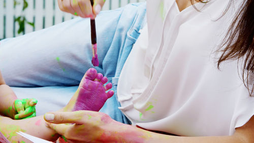 A young beautiful mother and her one-year-old daughter playing with finger paints in the garden