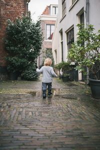 Rear view of boy walking on footpath during rainy season