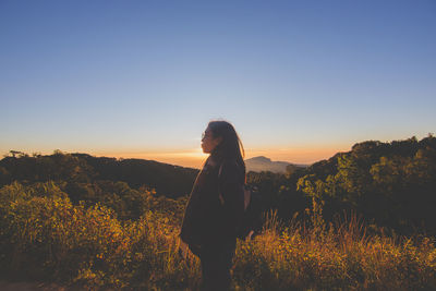 Woman standing on field against sky during sunset