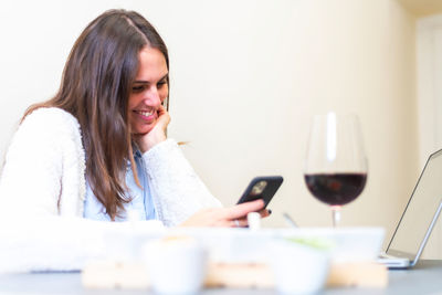 Young woman using phone while sitting on table