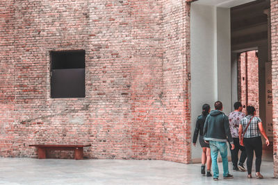 Rear view of people walking against brick wall