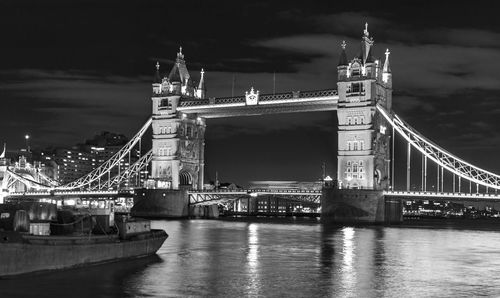 Illuminated bridge over river against sky in city at night