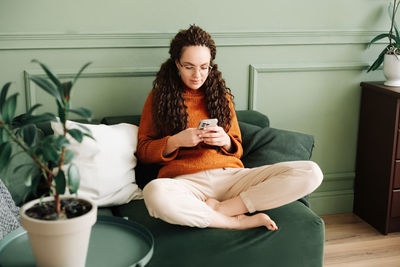 Happy woman relaxing on sofa using cell phone for shopping and social media at home - ecommerce and