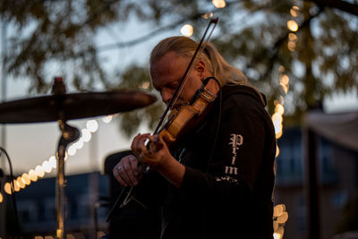 Side view of man playing violin against tree during sunset